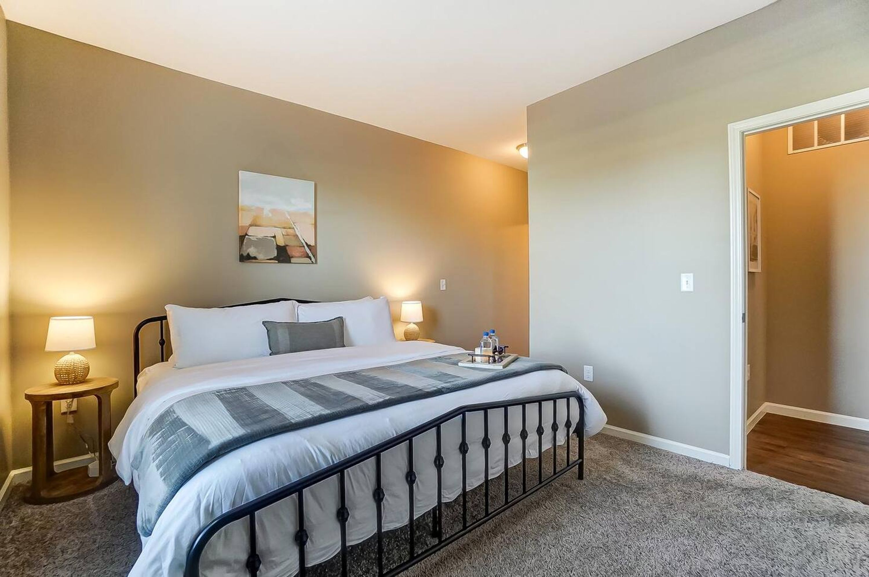 A neatly made bed with a striped blanket, two bedside lamps, and a small table with a lamp and a tray of items.
