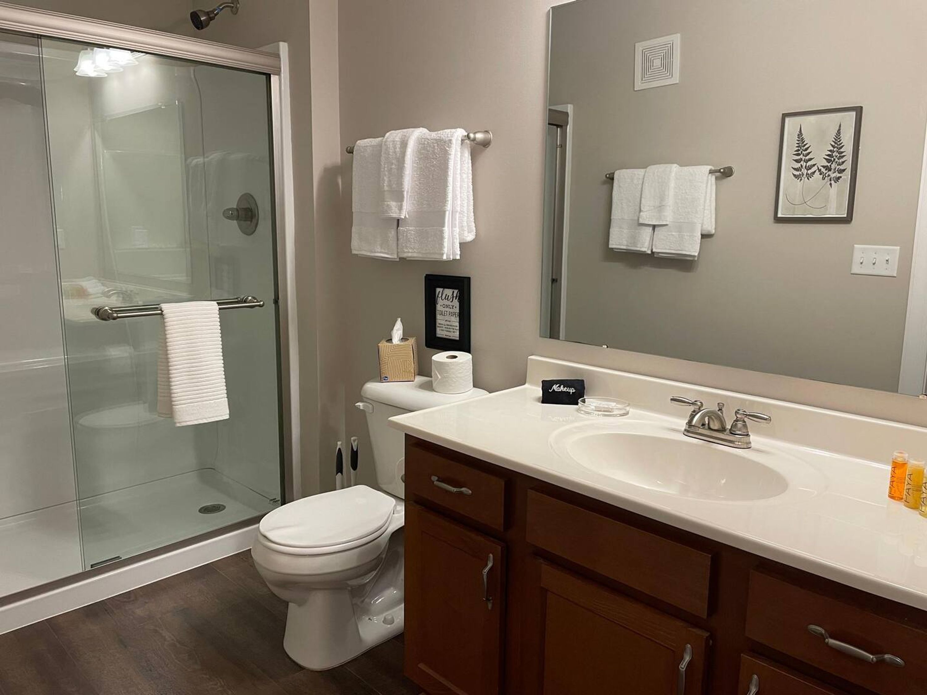 A modern bathroom with a glass shower enclosure, a toilet, a vanity with a sink, and a large mirror.
