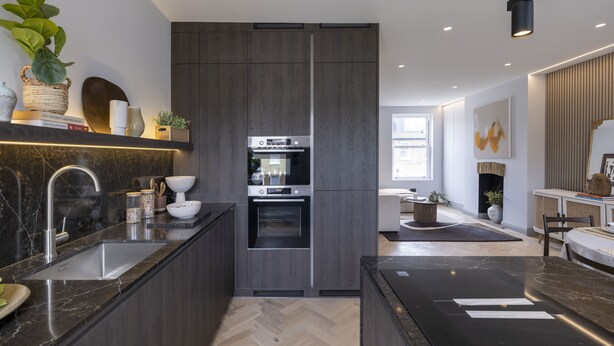 Una cocina moderna con armarios de madera oscura, horno empotrado y encimera de mármol.