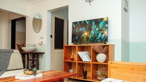 Ein Wohnzimmer mit Couch, Fernseher an der Wand und Bücherregal, inklusive Couchtisch aus Holz.