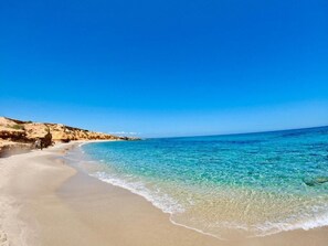 A beach with clear turquoise water, sandy shore, and rocky cliffs. - Beachfront Studio in Hergla – Stunning Sea View & Pool Access (Hergla)