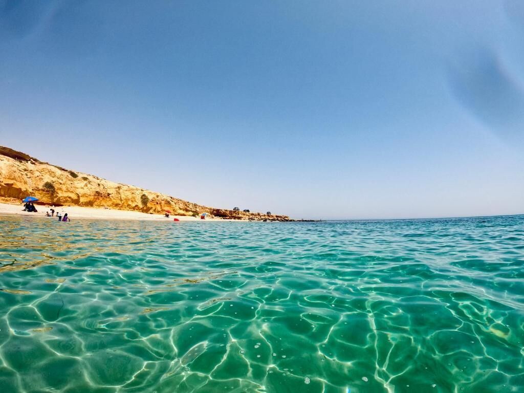 Ein Strand mit klarem türkisblauem Wasser und einem sandigen Ufer.