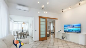 A modern living room with a sofa, a TV mounted on the wall, and a dining area with a table and chairs. - Olympic Vatican Home (Roma)