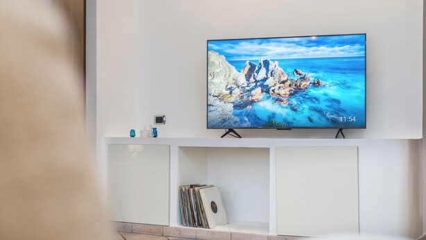 A flat-screen TV mounted on a white wall, displaying a scenic coastal image. - Olympic Vatican Home (Roma)
