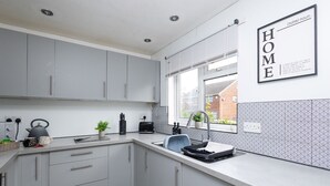 A modern kitchen with grey cabinets, a built-in oven, and a window with blinds.