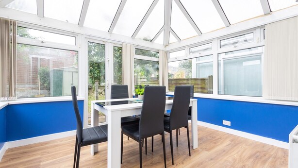 A conservatory with a white table and black chairs, large windows, and a blue wall.