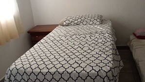 A small, single-bed room with a patterned bedspread, a wooden nightstand, and a window with curtains.