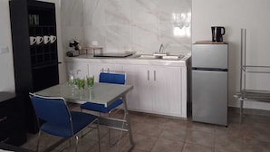 A compact kitchen with a marble backsplash, a sink, a refrigerator, and a dining area with blue chairs.