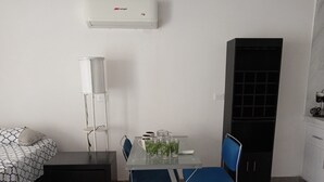 A small, modern room with a bed, a desk, a chair, a tall cabinet, and an air conditioner.
