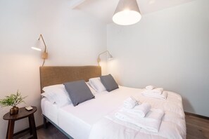 Een net opgemaakt bed met kussens, een nachtkastje met een lamp en een hangende lamp.