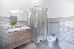 Uma casa de banho moderna com cabine de duche em vidro, lavatório, bidé e espelho.