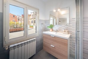 A bathroom with a window, a radiator, a sink with a mirror, and a shower.