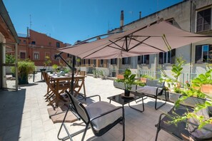 An outdoor patio with tables and chairs, a large umbrella, and potted plants.