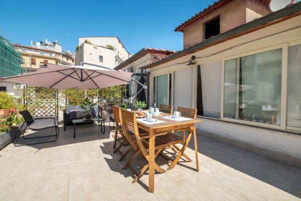 An outdoor patio with a wooden table and chairs, a grill, and a large umbrella. - Laura Roof Terrace Teatro dell'Opera (Roma)
