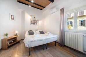 A bedroom with a bed, bedside table, lamp, framed picture, and a window with curtains.