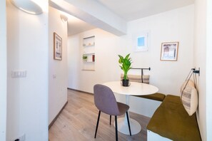 A modern, well-lit room with a round dining table, a single chair, a potted plant, and a bench with cushions.
