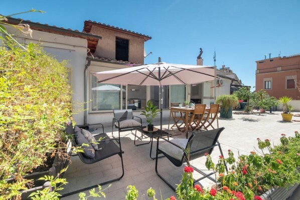 An outdoor patio with a table and chairs, a large umbrella, and potted plants.
