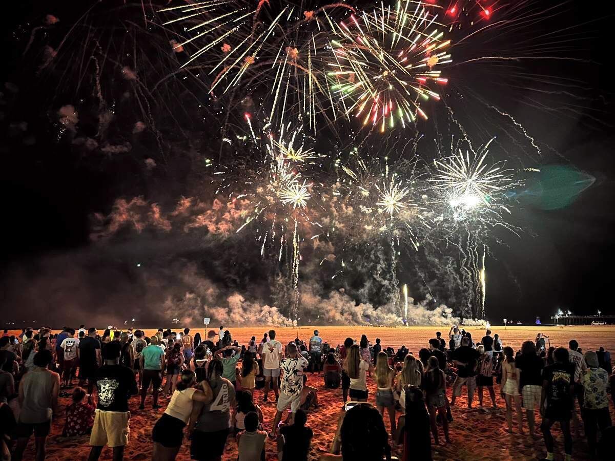 A beach with a crowd of people watching fireworks.