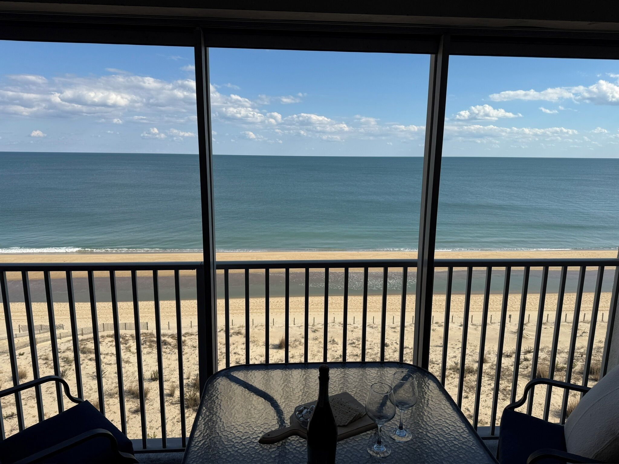 Uitzicht op een strand vanaf een balkon, met een tafel, stoelen, een fles en glazen.