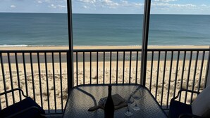 Blick auf einen Strand vom Balkon aus, mit Tisch, Stühlen, einer Flasche und Gläsern.