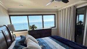 Ein Schlafzimmer mit einem großen Bett, einem Deckenventilator, Meerblick durch ein Fenster und einer Schiebeglastür.