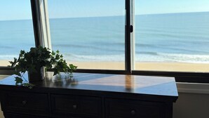 Blick auf das Meer durch ein Fenster, mit einer Pflanze auf einer Kommode.