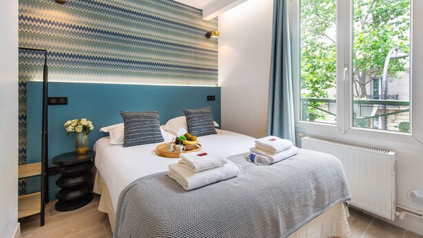 Una camera d'albergo moderna con un letto grande, un tavolino con un vaso di fiori, un vassoio con prodotti per la colazione e vista sugli alberi dalla finestra.