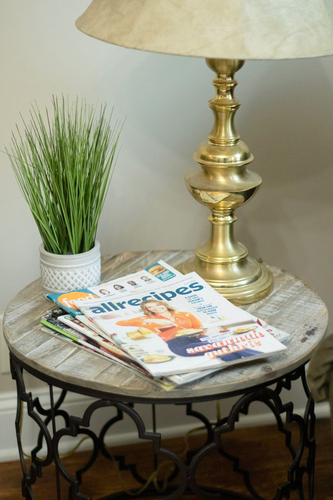 Une table ronde avec un magazine, une plante en pot et une lampe.