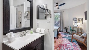 A bathroom with a large mirror, two sinks, and a white vanity. There is a colorful rug in the adjacent room. - Your Slice of Paradise Near Clearwater Beach – 1BR Condo (Clearwater)