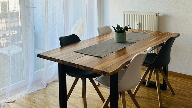 Een eetruimte met een houten tafel, zwarte stoelen, een potplant en transparante gordijnen.