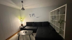 Een moderne woonkamer met een hoekbank, een bijzettafeltje, een vloerlamp en een tv-meubel aan de muur.