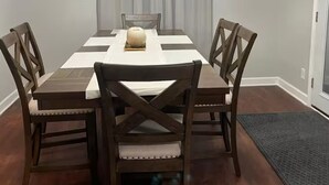 A dining room with a rectangular table, four wooden chairs, a chandelier, and a grey curtain.