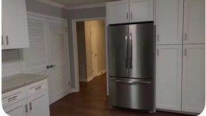 A kitchen with white cabinets, a stainless steel refrigerator, and a wooden countertop.