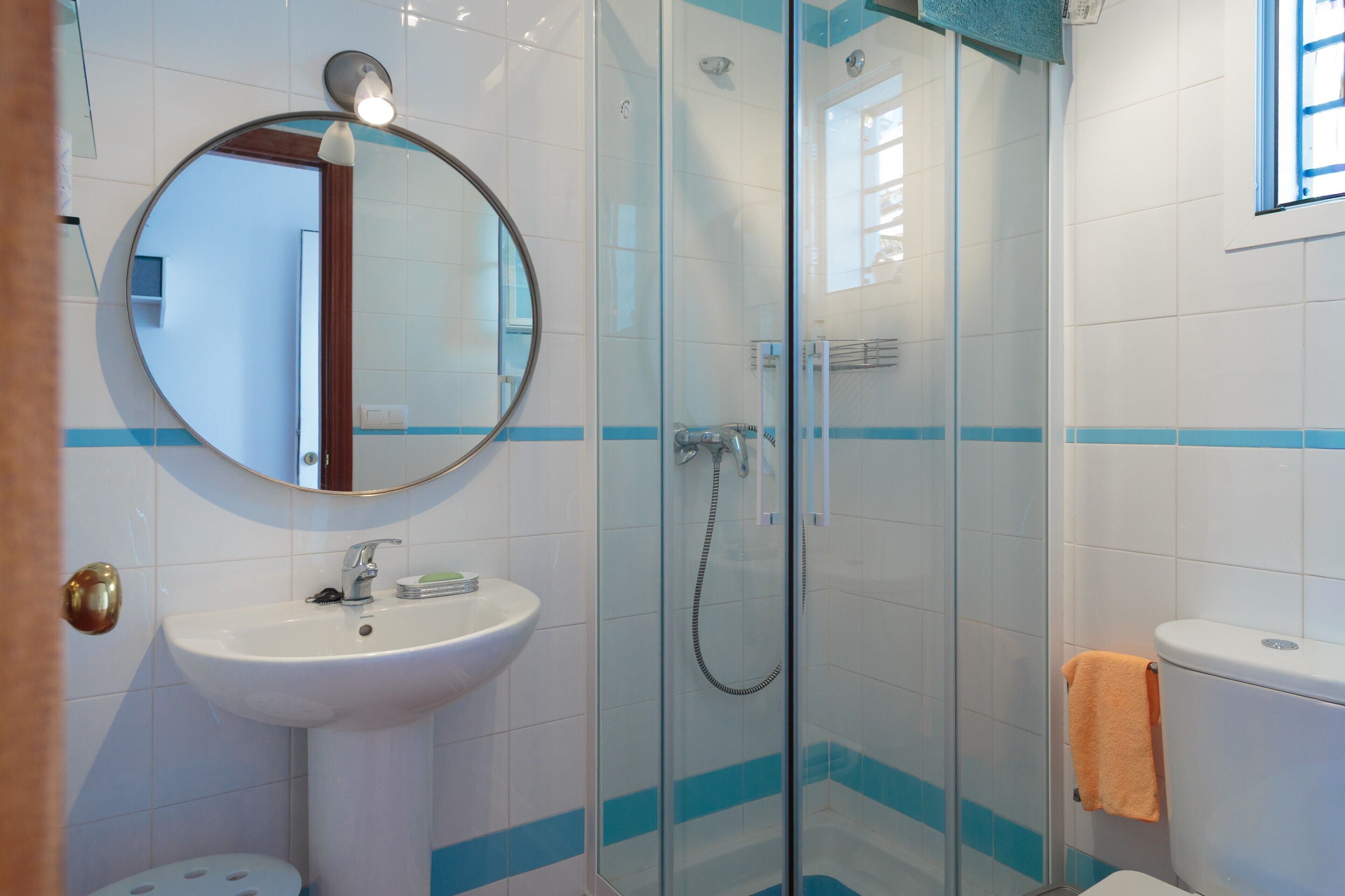 A bathroom with a round mirror, a sink, a glass-enclosed shower, and a toilet.
