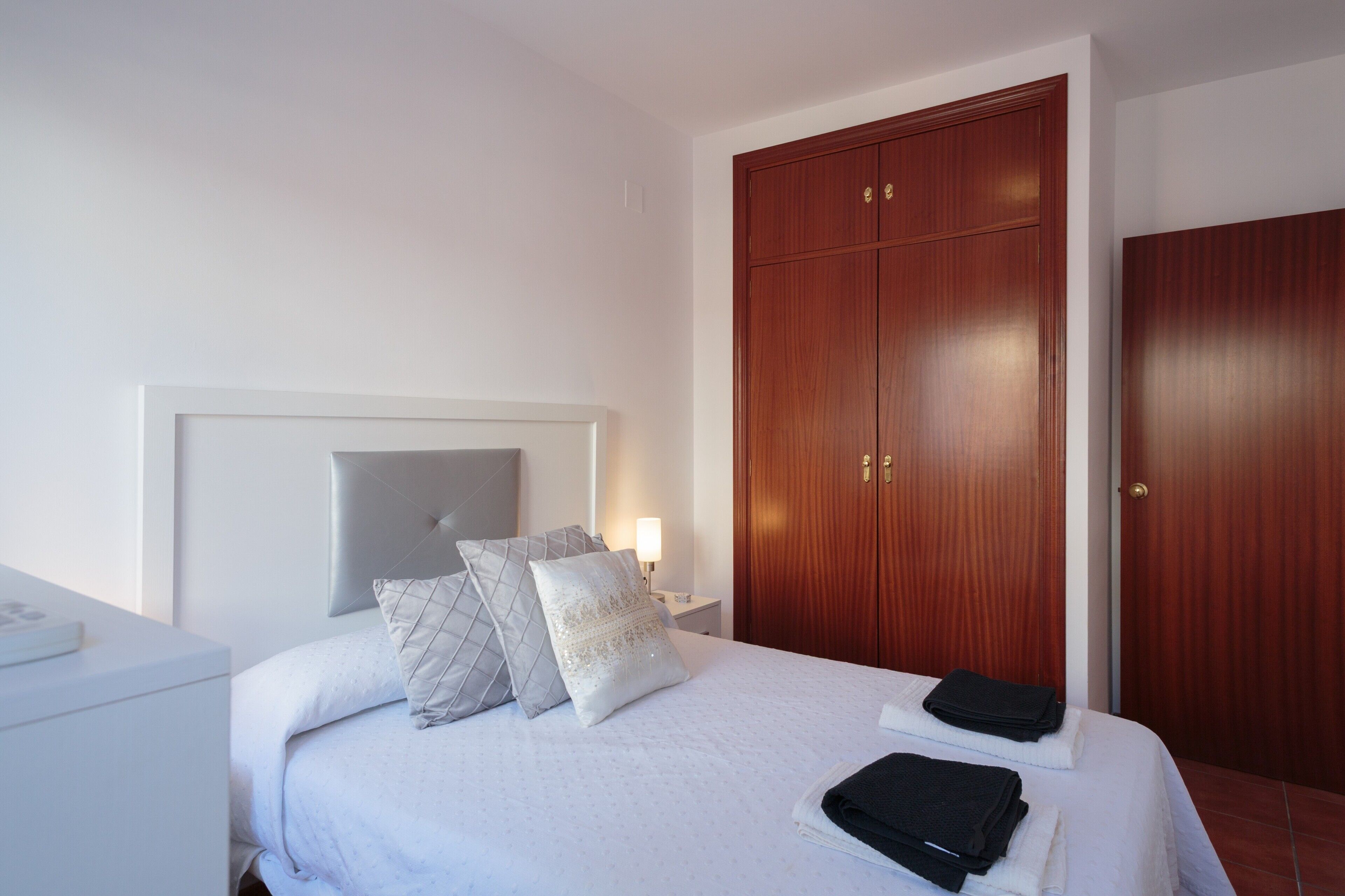 Ein Hotelzimmer mit Bett, Nachttisch, Holzschrank und weißem Beistelltisch.