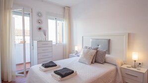 Une chambre à coucher comprenant un lit, des tables de chevet, une commode, une coiffeuse et une porte-fenêtre coulissante donnant sur un balcon.