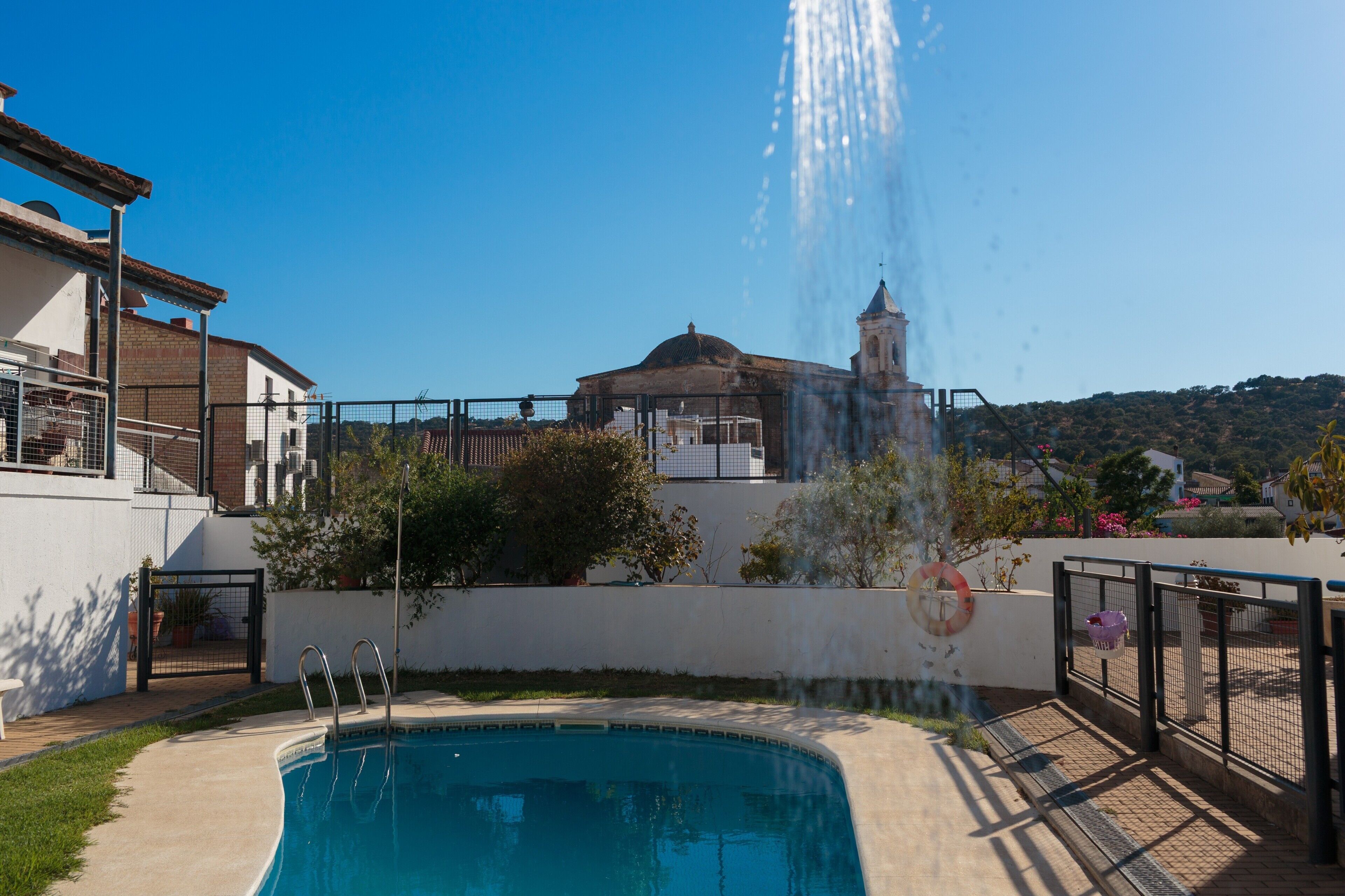 A swimming pool with a fountain, a white building with a dome, and a church with a bell tower in the background.