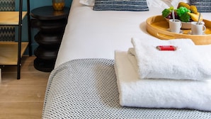 Habitación de hotel ordenada con cama, almohadas, bandeja con frutas y vasos, jarrón con flores y pared con diseño en zigzag.