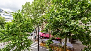 Vista de calle con un café bajo un toldo rosa, un paso de cebra y un edificio de diseño moderno.