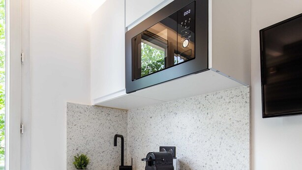 Una cocina compacta con muebles blancos, microondas integrado, lavamanos y una pequeña encimera.