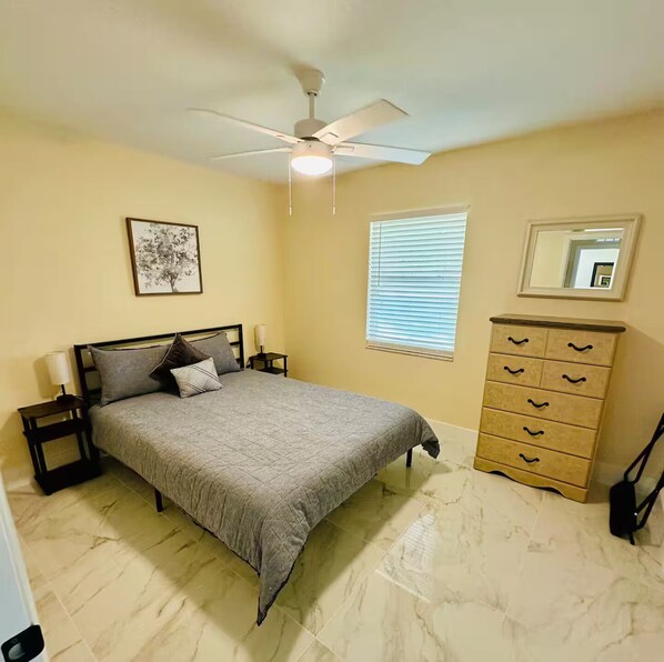A bedroom with a bed, nightstands, a dresser, a ceiling fan, a window with blinds, and a wall-mounted mirror. - The 98 House Minutes from WEC, OBS, FAST & HITS. Located off of W HWY 40! (Ocala)