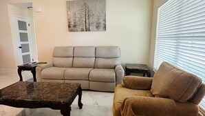 A living room with a beige sofa, a brown armchair, a marble coffee table, and a painting on the wall. - The 98 House Minutes from WEC, OBS, FAST & HITS. Located off of W HWY 40! (Ocala)