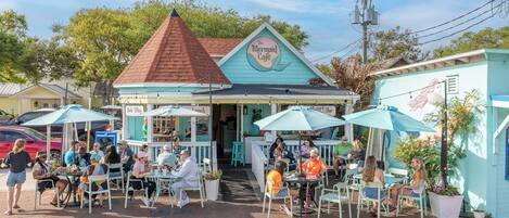 A seaside café with outdoor seating and a colorful sign.