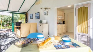 Quarto com mesa de jantar posta, comida, televisão e vista para o jardim.