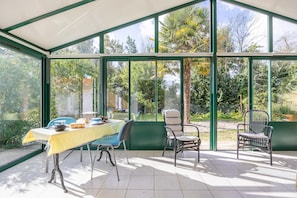 Ein Wintergarten mit Tisch und Stühlen, großen Fenstern und Blick auf den Garten.