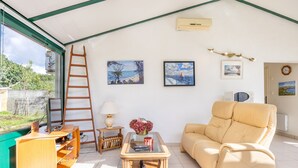 Quarto com sofá, escrivaninha de madeira, mesinha de centro de vidro e quadros nas paredes.