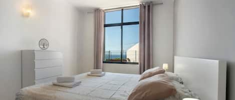 A modern bedroom with a large window, a bedside table with a lamp, and a headboard.