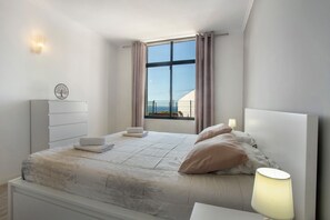 A modern bedroom with a large window, a bedside table with a lamp, and a headboard. - Apartment 'Refúgio Na Cidade 104' with Wi-Fi (Funchal)