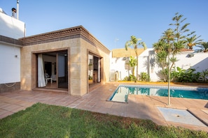 A poolside area with a patio, a small building with an open door, and a swimming pool.