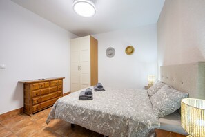 A bedroom with a bed, a dresser, a wardrobe, and two wall-mounted lamps.